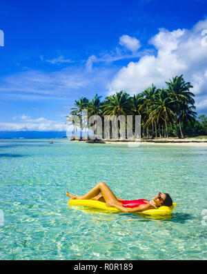 Jeune femme en maillot rouge sur jaune soleil matelas d'air, flottant sur la mer des Caraïbes, la plage tropicale, palmiers, Guadeloupe, French West Indies, Banque D'Images