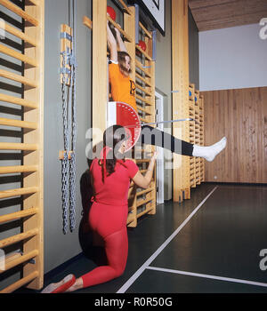 Gymnastique scolaire en 1970s. Un enseignant aide une jeune fille pendant la classe de gymnastique. Elle mesure l'angle des jambes à l'aide d'une échelle. Suède 1972 Banque D'Images