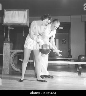 Bowling dans le 1950s. Un homme avec trois jeunes femmes dans une piste de bowling. Elles sont vêtues de jupes et de pulls à rayures courtes. Les trois filles sont toutes des actrices de théâtre : Ingrid Björk, UllaCarin Rydén et BRITA Ulfberg. Les spectacles Ewert Ekström les instruit dans le bowling. Il était joueur professionnel de bowling en 1930s et est actuellement instructeur et propriétaire du club de bowling. 1950. Suède photo Kristoffersson réf. AY36-12 Banque D'Images