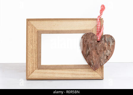 Emptty cadre photo en bois avec de l'écorce en forme de coeur debout sur une table en bois blanc contre mur isolé Banque D'Images