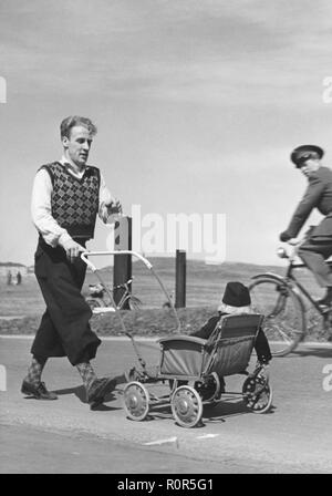 Le père et l'enfant dans les années 40. Un homme portant des années 1940, typique de la mode d'une presse à pantalons est poussant une poussette avec son enfant. Il est marcher pour un événement de bienfaisance 1942 Banque D'Images