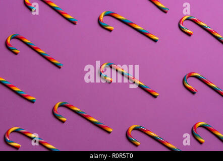 Image Noël minimaliste avec des cannes de bonbon de couleur arc-en-ciel, affiché dans un modèle sur un fond mauve. Banque D'Images