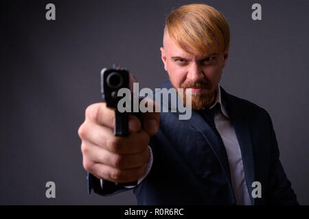 Homme barbu avec pistolet contre l'arrière-plan gris Banque D'Images