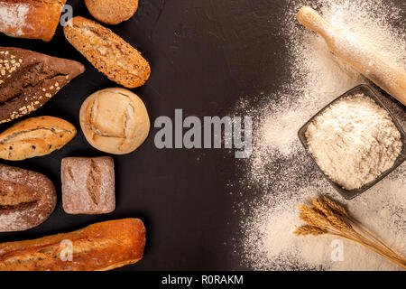 D'en haut photo de pain buns, loafs, bol de farine sur le tableau noir avec le matériel roulant et de blé rose Banque D'Images