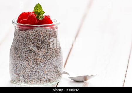 Photo de gros plan petit verre avec sweet chia seeds au lait garnie de framboises fraîches sur la table en bois blanc Banque D'Images