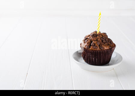 Anniversaire capkakes ou muffins au chocolat et des bougies sur une table en bois blanc. Arrière-plan blanc. Un aliment sucré. Ambiance de fête copie espace télévision lay Banque D'Images