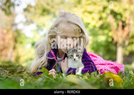 Belle fille blonde avec cat et couché ensemble sur l'herbe dans le temps d'automne Banque D'Images