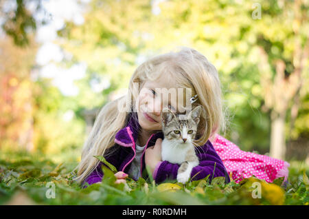Belle fille blonde avec cat et couché ensemble sur l'herbe dans le temps d'automne Banque D'Images