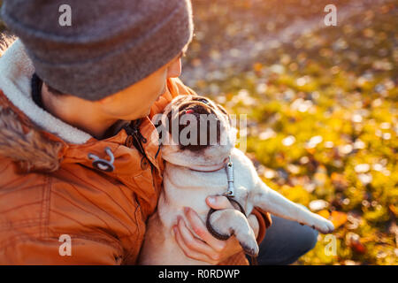 Holding maître chien pug en mains en automne parc. Chiot heureux à la recherche sur l'homme et montrant la langue. Banque D'Images