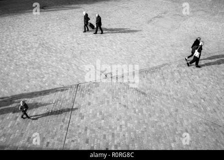 Les gens d'en haut trouble méconnaissable marche sur un espace ouvert carré avec la projection des ombres sur le sol Banque D'Images
