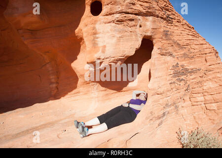 Femme hiker relaxing dans une alcôve de la formation rocheuse de ruches en Vallée de Feu park NEVADA USA Banque D'Images