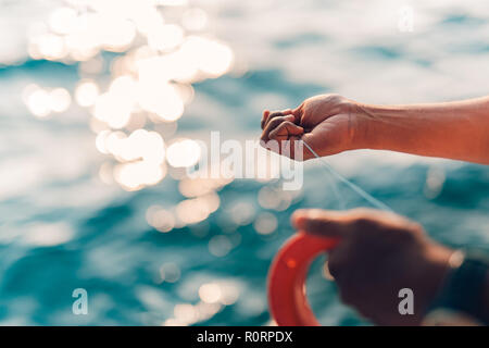 Bien utilisé la ligne à main et bobine de pêche en mer tropicale. Arrière-plan de la mer trouble. Le sport et les loisirs liés à l'eau contexte Banque D'Images