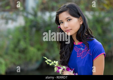 Jeune femme en bleu vietnamiens Ao Dai holding Flowers en regardant la caméra. Banque D'Images