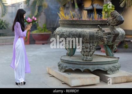 Young Asian woman making un ex-voto de fleurs rose frais à un temple bouddhiste en plein air remplie de bâtons d'encens ou de brûlure joss Banque D'Images