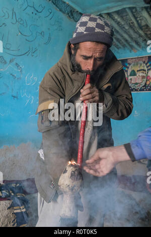 Homme qui fume du haschich avec un bong près de la tombe d'un saint soufi, ancienne Balkh, au nord de l'Afghanistan Banque D'Images