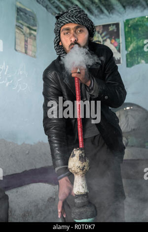 Homme qui fume du haschich avec un bong près de la tombe d'un saint soufi, ancienne Balkh, au nord de l'Afghanistan Banque D'Images