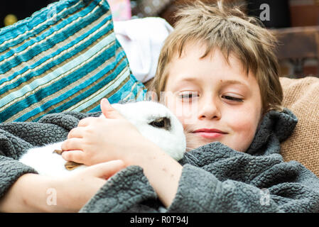 Un beau happy smiling little boy with autism, Aspergers syndrome et tdah de câliner son animal préféré le lapin dans le jardin à la maison Banque D'Images