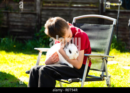 Un beau happy smiling little boy with autism, Aspergers syndrome et tdah de câliner son animal préféré le lapin dans le jardin à la maison Banque D'Images