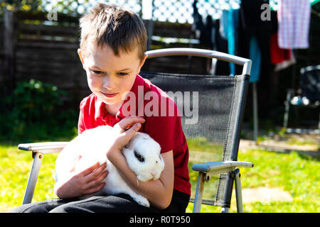 Un beau happy smiling little boy with autism, Aspergers syndrome et tdah de câliner son animal préféré le lapin dans le jardin à la maison Banque D'Images