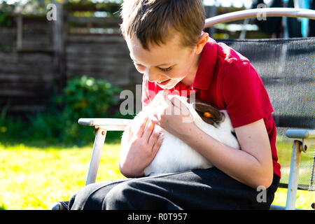 Un beau happy smiling little boy with autism, Aspergers syndrome et tdah de câliner son animal préféré le lapin dans le jardin à la maison Banque D'Images