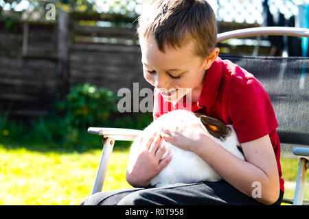 Un beau happy smiling little boy with autism, Aspergers syndrome et tdah de câliner son animal préféré le lapin dans le jardin à la maison Banque D'Images