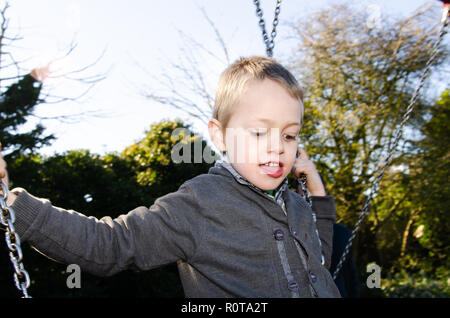 Un beau petit garçon avec le TDAH, l'Autisme, syndrome d'Aspergers joue heureusement sur une balançoire dans le soleil de l'été Banque D'Images