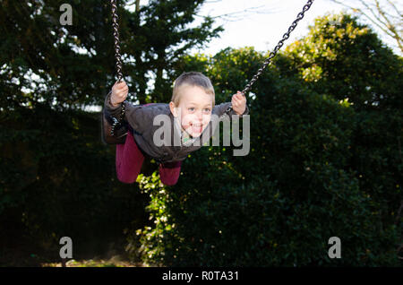 Un beau petit garçon avec le TDAH, l'Autisme, syndrome d'Aspergers joue heureusement sur une balançoire dans le soleil de l'été Banque D'Images