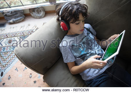 Garçon Latinx avec casques using digital tablet on sofa