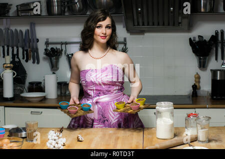 Belle fille de cuisiniers dans la cuisine, cupcakes en mains, ressemble à l'appareil photo Banque D'Images