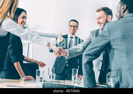 Multicultural businesspeople shaking hands in conference hall tandis que chef d'équipe showing thumb up Banque D'Images