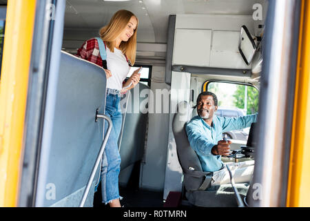 Teen schoolgirl walking par autobus scolaire tout en souriant à son pilote principal Banque D'Images