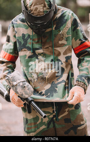 Le joueur avec le marqueur de paintball gun regardant couverts par camouflage paintball splash en plein air Banque D'Images