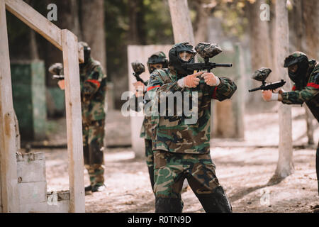 L'équipe de paintball en uniforme et des masques de protection par le tir des fusils à balles à l'extérieur Banque D'Images