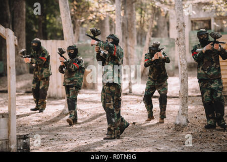 L'équipe de paintball en uniforme et des masques de protection par le tir des fusils à balles à l'extérieur Banque D'Images