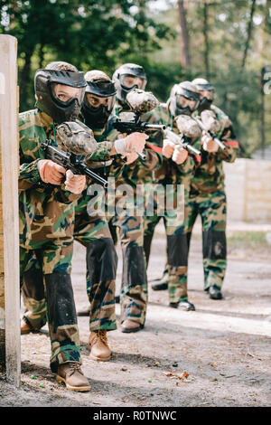 Paintball femelle joueur tenant des armes à feu de gabarit avec son équipe en des masques de protection et camouflage le paintball en plein air Banque D'Images
