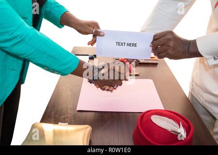 Suis homme et femme d'affaires africaine se serrer la main qu'ils donnent et reçoivent de l'enveloppe ordinaire (pour l'ajout de texte) sur une table de bureau avec un fond blanc. Banque D'Images