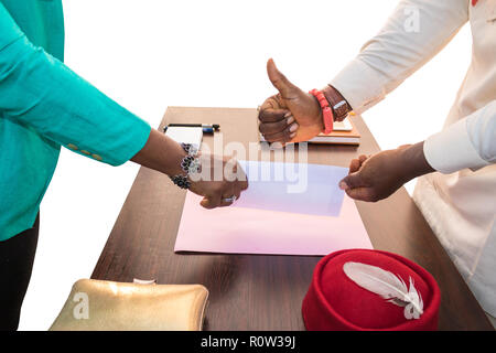 Suis homme et femme d'affaires africaine se serrer la main qu'ils donnent et reçoivent de l'enveloppe ordinaire (pour l'ajout de texte) alors qu'il n'Thumbs up sur un bureau avec table Banque D'Images