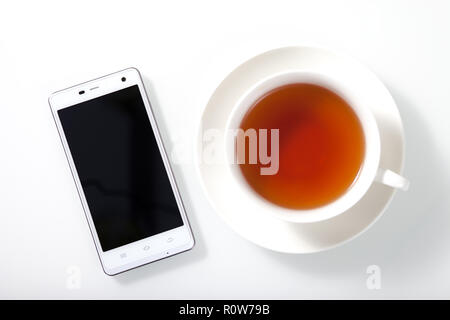 Smartphone blanc et d'une tasse de thé sur la table en verre blanc avec des ombres Banque D'Images