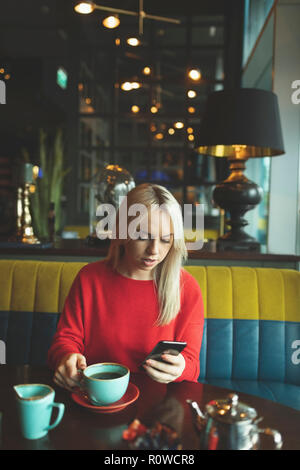 Woman using mobile phone while having coffee Banque D'Images