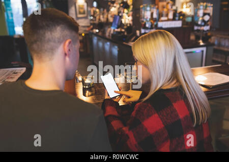 Couple discutant sur téléphone mobile au comptoir du bar Banque D'Images