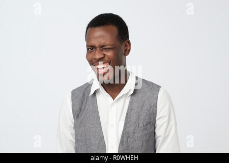 Jeune homme africain portant une chemise blanche et gilet dans la bonne humeur flirt, tout sourire et clignant de l'oeil Banque D'Images