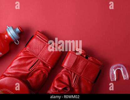 Gants de boxe en cuir rouge, une bouteille d'eau en plastique et capuchon en silicone pour les dents sur un fond rouge, copy space Banque D'Images