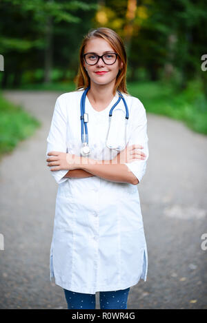 Une jeune fille qui est médecin se trouve à l'extérieur, bras croisés sur le ventre. Banque D'Images