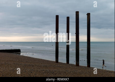 Jogger running on beach à côté de piliers de West Pier de Brighton, en ruine Banque D'Images