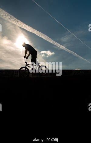 Un rider de bmx au Plaza, Central Forest Park à Stoke on Trent haut perchés et tombé sur une bande en silhouette au coucher du soleil Banque D'Images