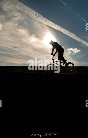 Un rider de bmx au Plaza, Central Forest Park à Stoke on Trent haut perchés et tombé sur une bande en silhouette au coucher du soleil Banque D'Images