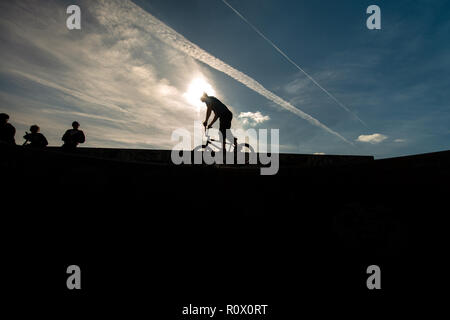 Un rider de bmx au Plaza, Central Forest Park à Stoke on Trent haut perchés et tombé sur une bande en silhouette au coucher du soleil Banque D'Images