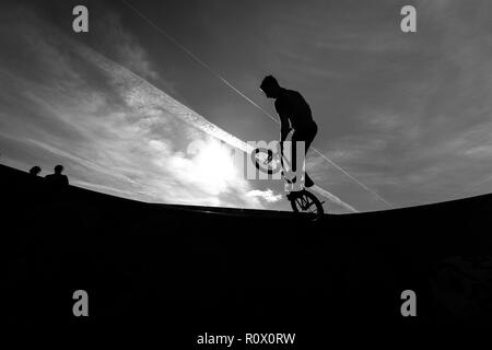 Un rider de bmx au Plaza, Central Forest Park à Stoke on Trent haut perchés et tombé sur une bande en silhouette au coucher du soleil Banque D'Images