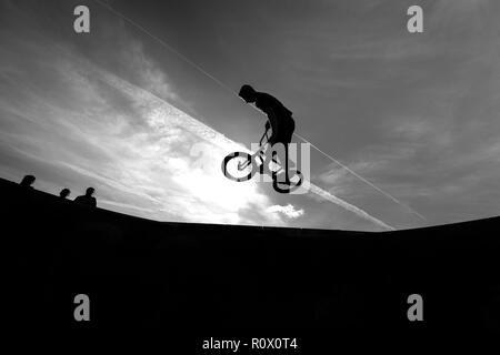 Un rider de bmx au Plaza, Central Forest Park à Stoke on Trent haut perchés et tombé sur une bande en silhouette au coucher du soleil Banque D'Images