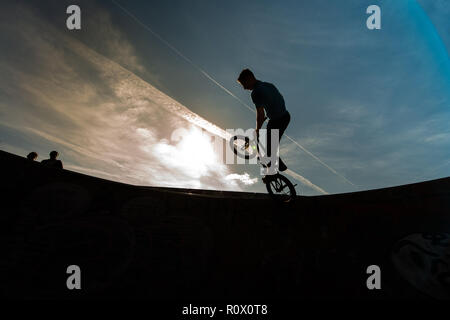 Un rider de bmx au Plaza, Central Forest Park à Stoke on Trent haut perchés et tombé sur une bande en silhouette au coucher du soleil Banque D'Images